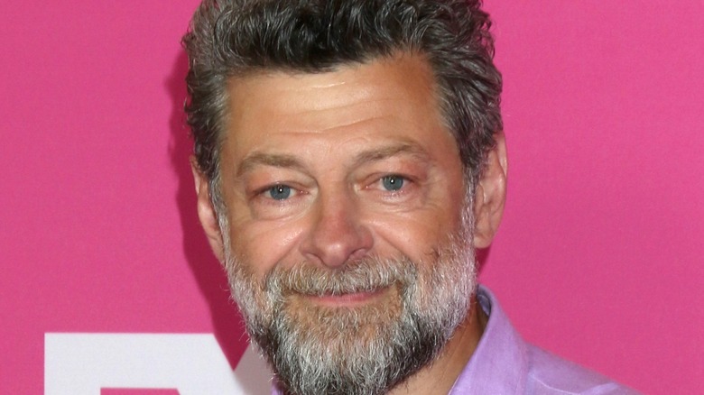 Andy Serkis with gray beard smiling pink background