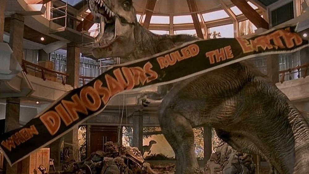 A Tyrannosaurus Rex roars inside a building while a banner reading "when dinosaurs walked the Earth" falls