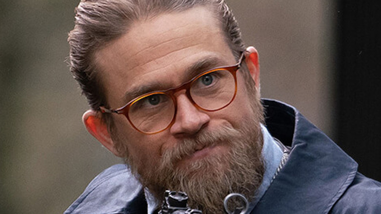 Charlie Hunnam wearing glasses and holding gun